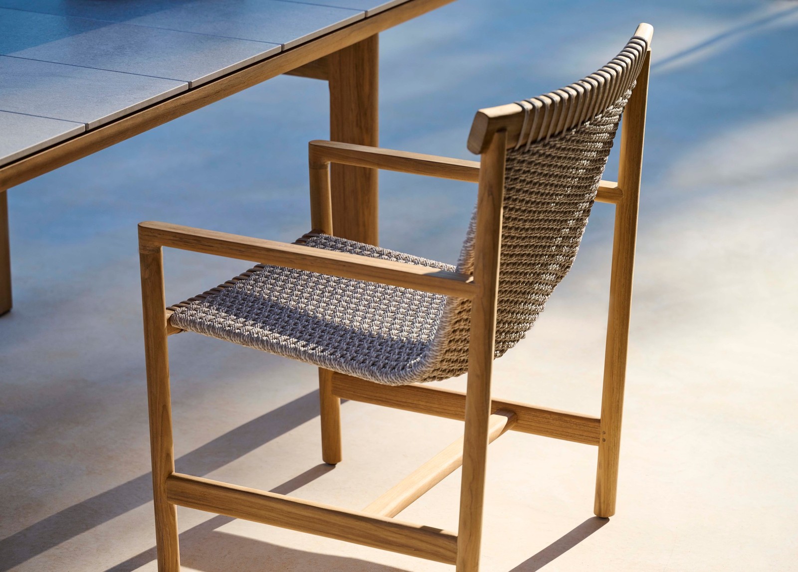 01-elara-teak-woven-outdoor-dining-chair-hero Elara teak and woven outdoor dining chair beside a dining table