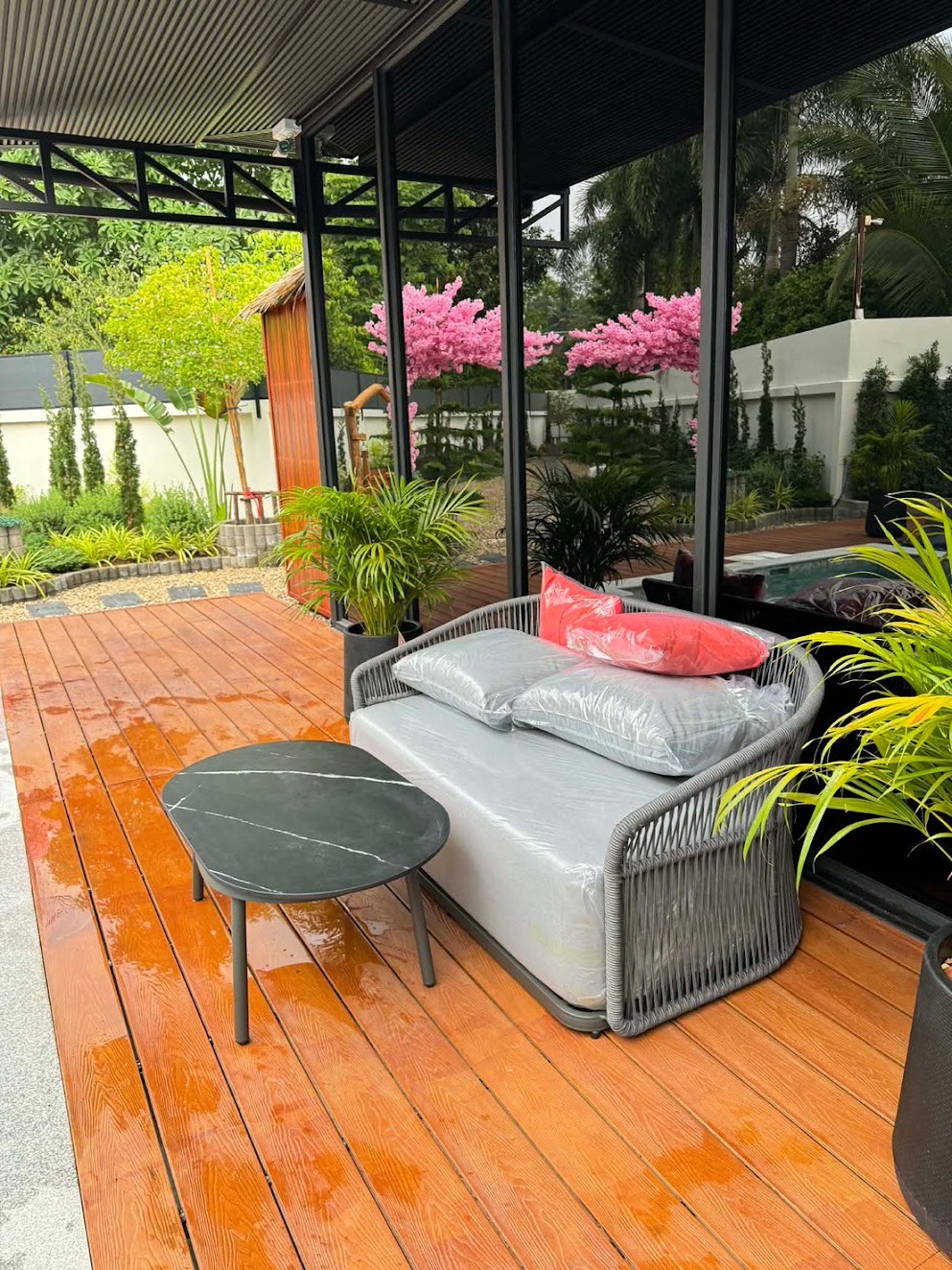 Grey outdoor loveseat and round table on a planted wooden terrace, Bunise order GF-000445