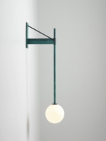 Verdigris green wall lamp illuminated against a pale wall.