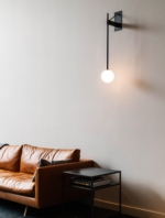Black globe wall lamp above a tan sofa and dark side table.