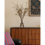 Left side of the wooden sideboard styled with a vase and framed artwork.