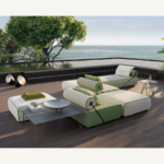Green and cream modular outdoor sofa with cylindrical back cushions and slim diagonal supports on a sea-facing terrace.