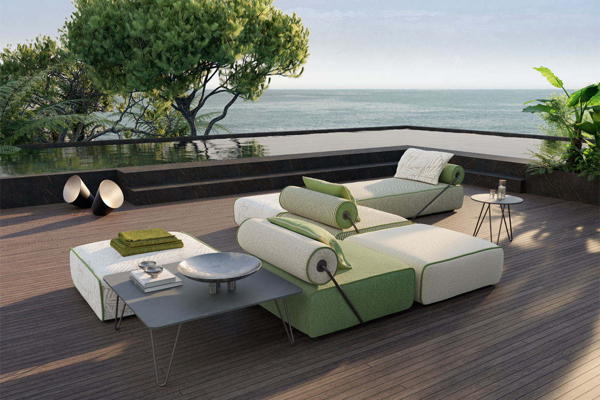 Green and cream modular outdoor sofa with cylindrical back cushions on a sea-facing terrace.