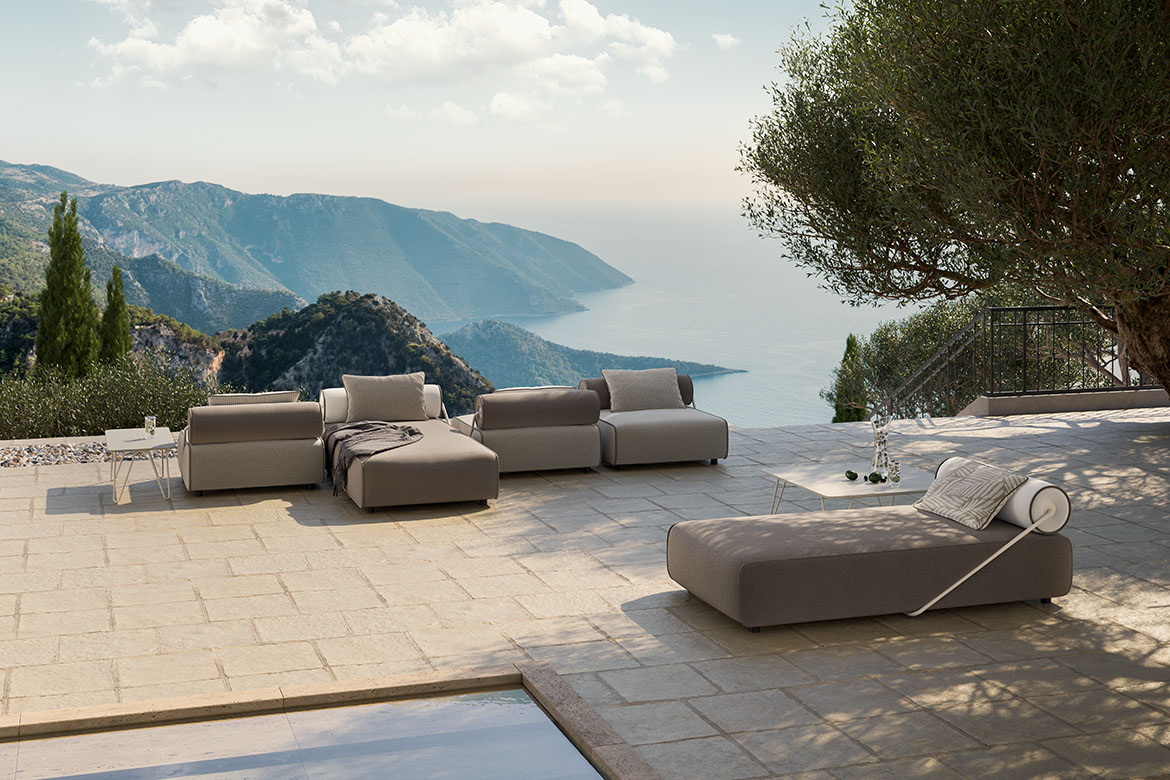 Design reference: Neutral modular seating and a separate chaise on a stone terrace overlooking the sea.